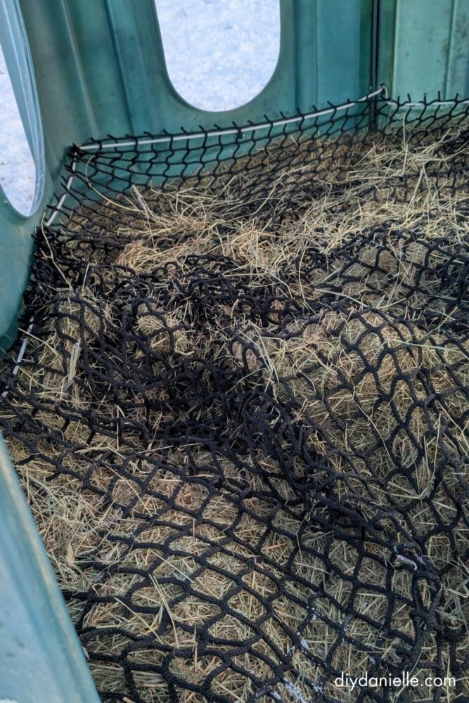 Hay Hut flipped upside down with a pallet underneath and a round bale placed inside before the Hay Hut and net are flipped back over.