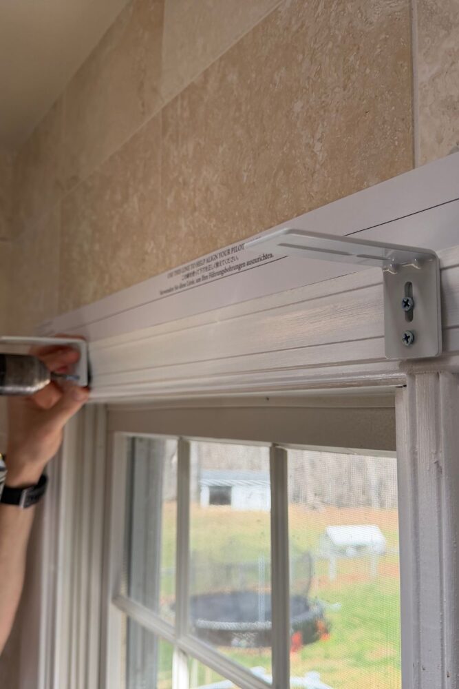 Screw in the long brackets. They can attach to the window trim or to the wall above the window... in this case, we didn't want to screw into the tile so we used the window trim.